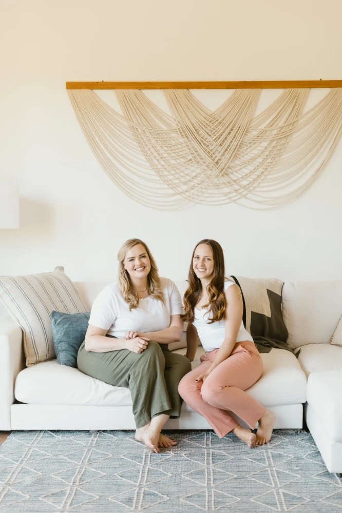 two women sitting on luxurious lounge with artwork behind them